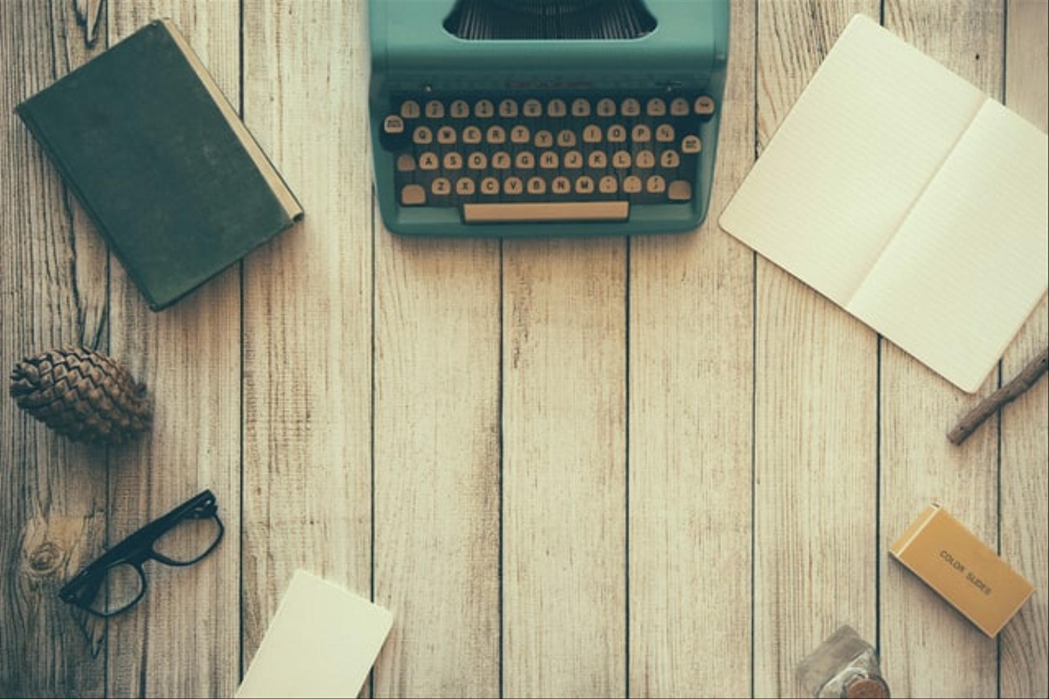 A placeholder image showing a typewriter and books on a wooden desk